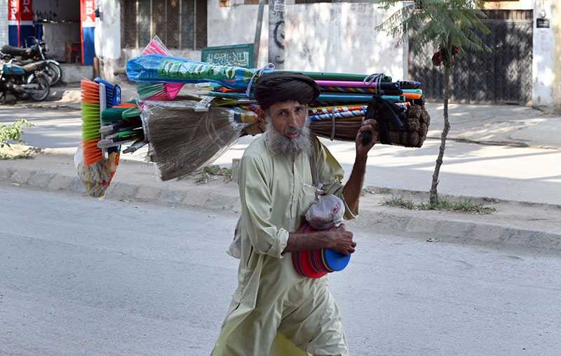 Elderly Vendor Carries Cleaning Tools Along Roadside